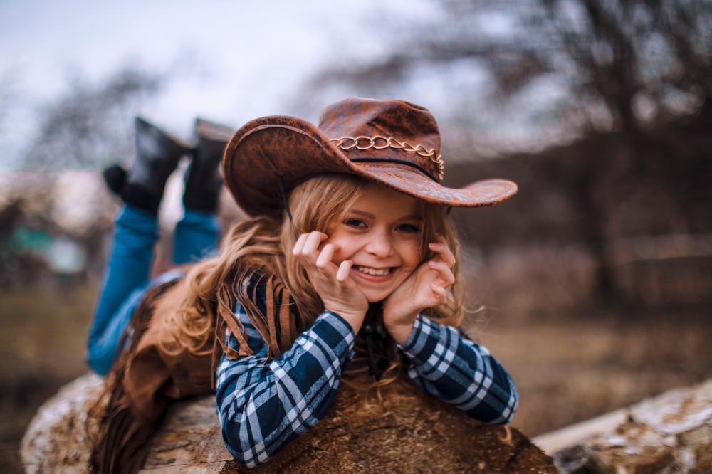 A smiling child in a cowboy hat on top of a rock